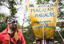 Autoroute A69, le droit tordu de l’État Un homme masqué durant une manifestation contre l'autoroute A69 avec une banderoles où est écrit "Non à l'A69, Macadam massacre." puis en-dessous : "Bifurquons sur les chemins de traverse."